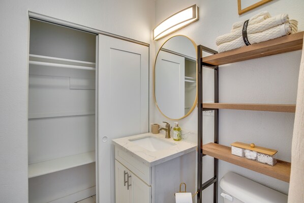 A bathroom with a white vanity, a mirror, a shelf with towels, and a toilet.