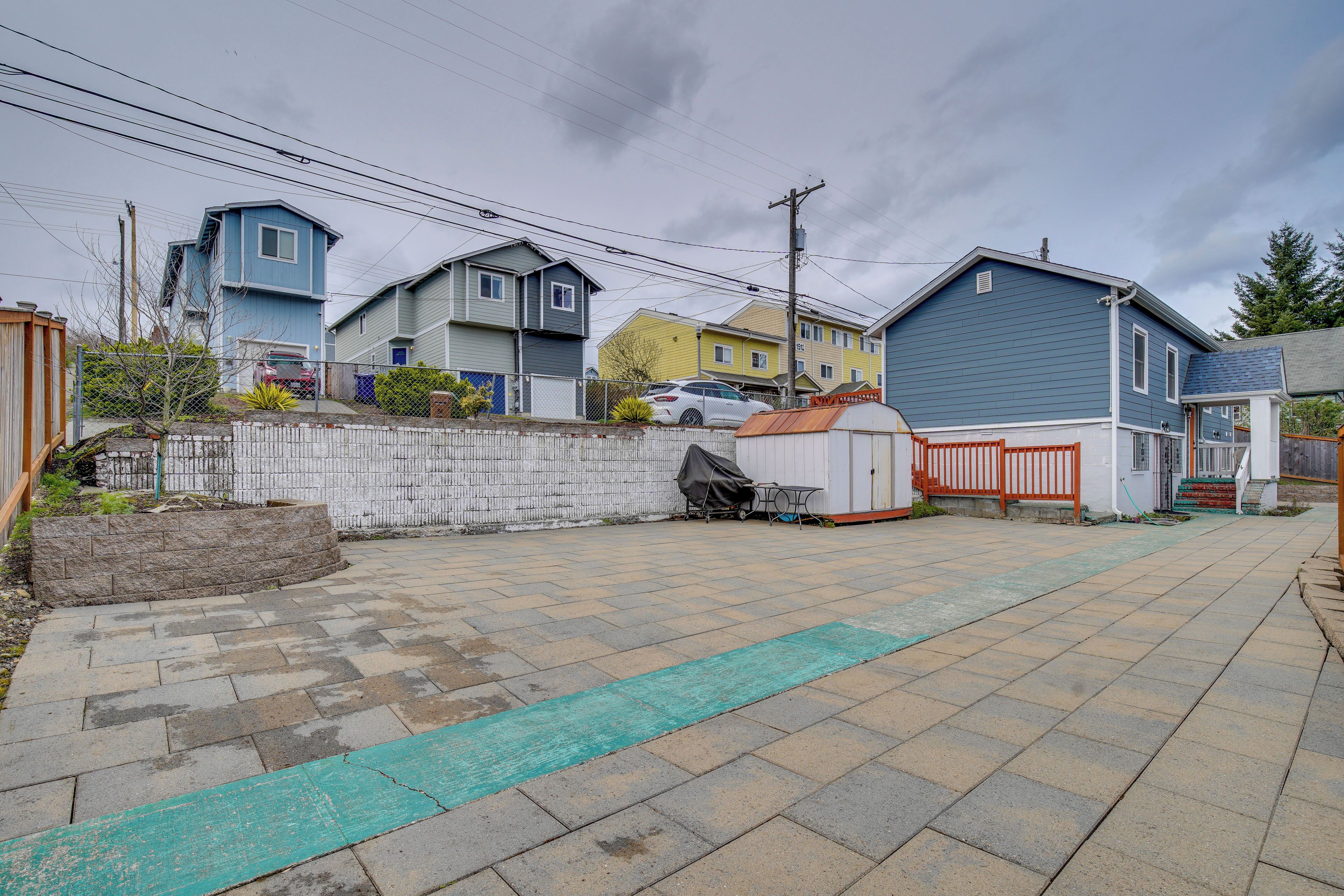 A residential area with a paved driveway, a fenced yard, and houses with different architectural styles.