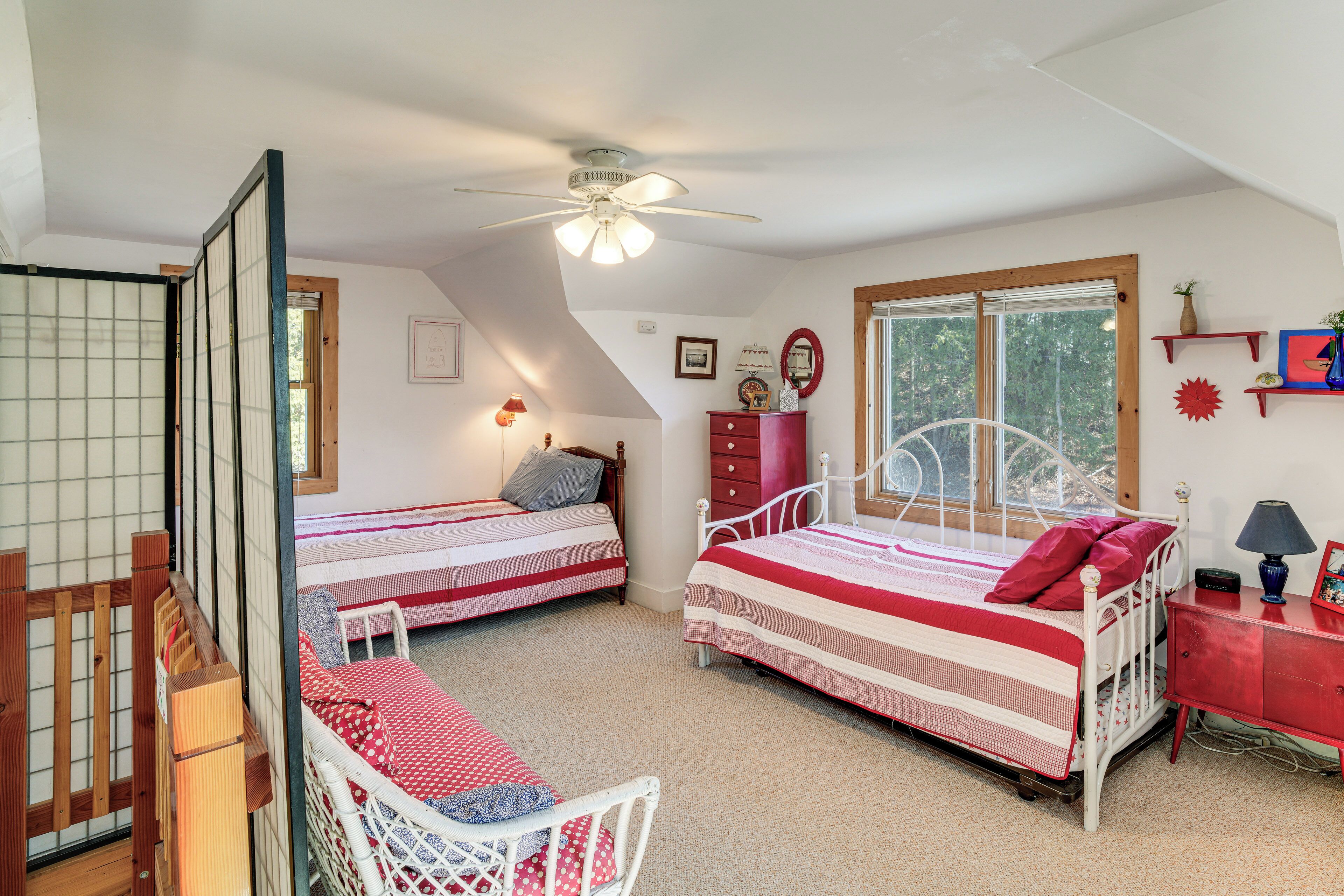 Une chambre avec deux lits, une chaise en bois, une commode et une fenêtre.