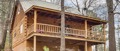 A log cabin with a balcony, surrounded by trees.