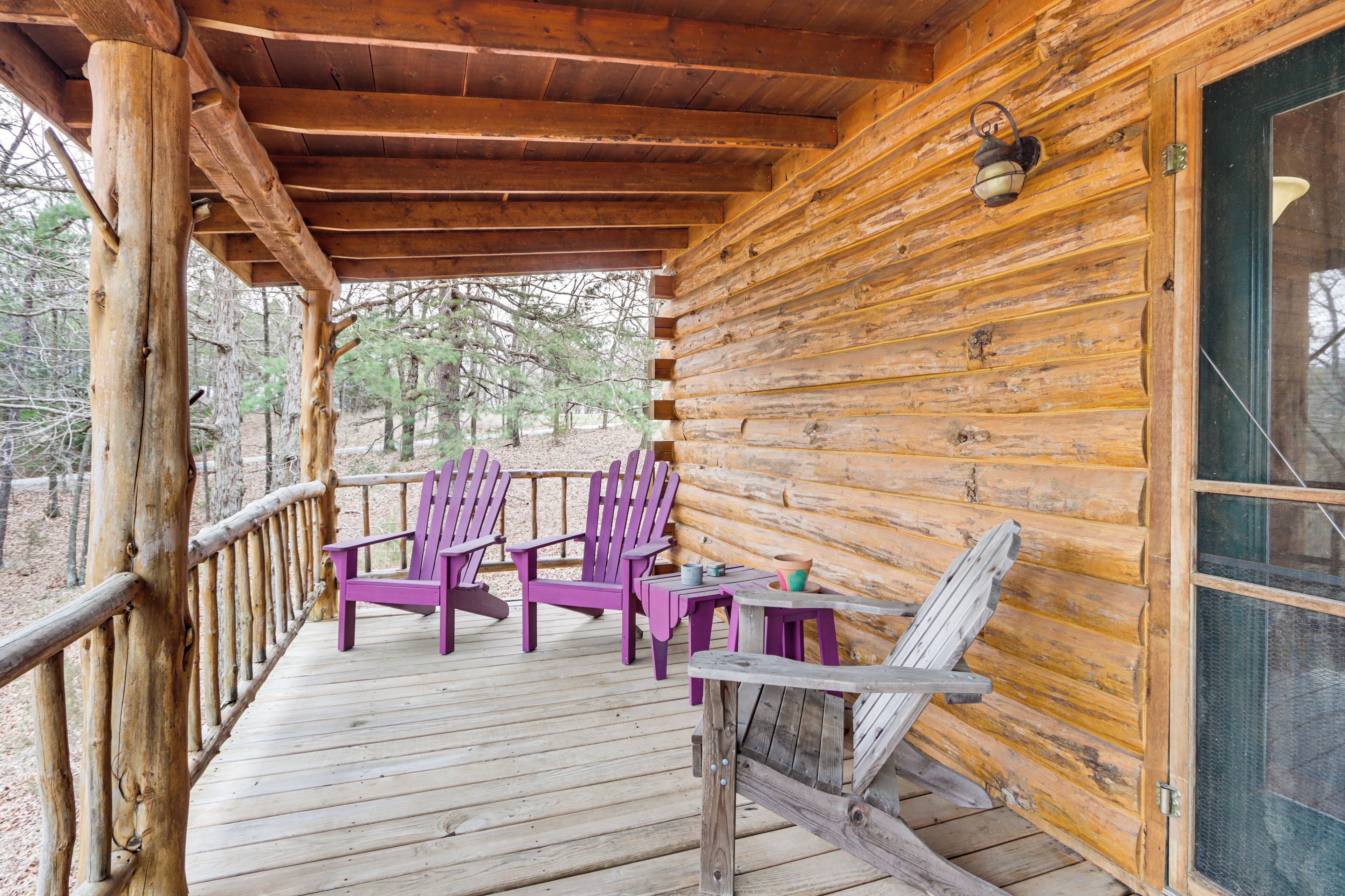 Una cabaña de madera con un porche, dos sillas Adirondack moradas, una mesa y una ventana.
