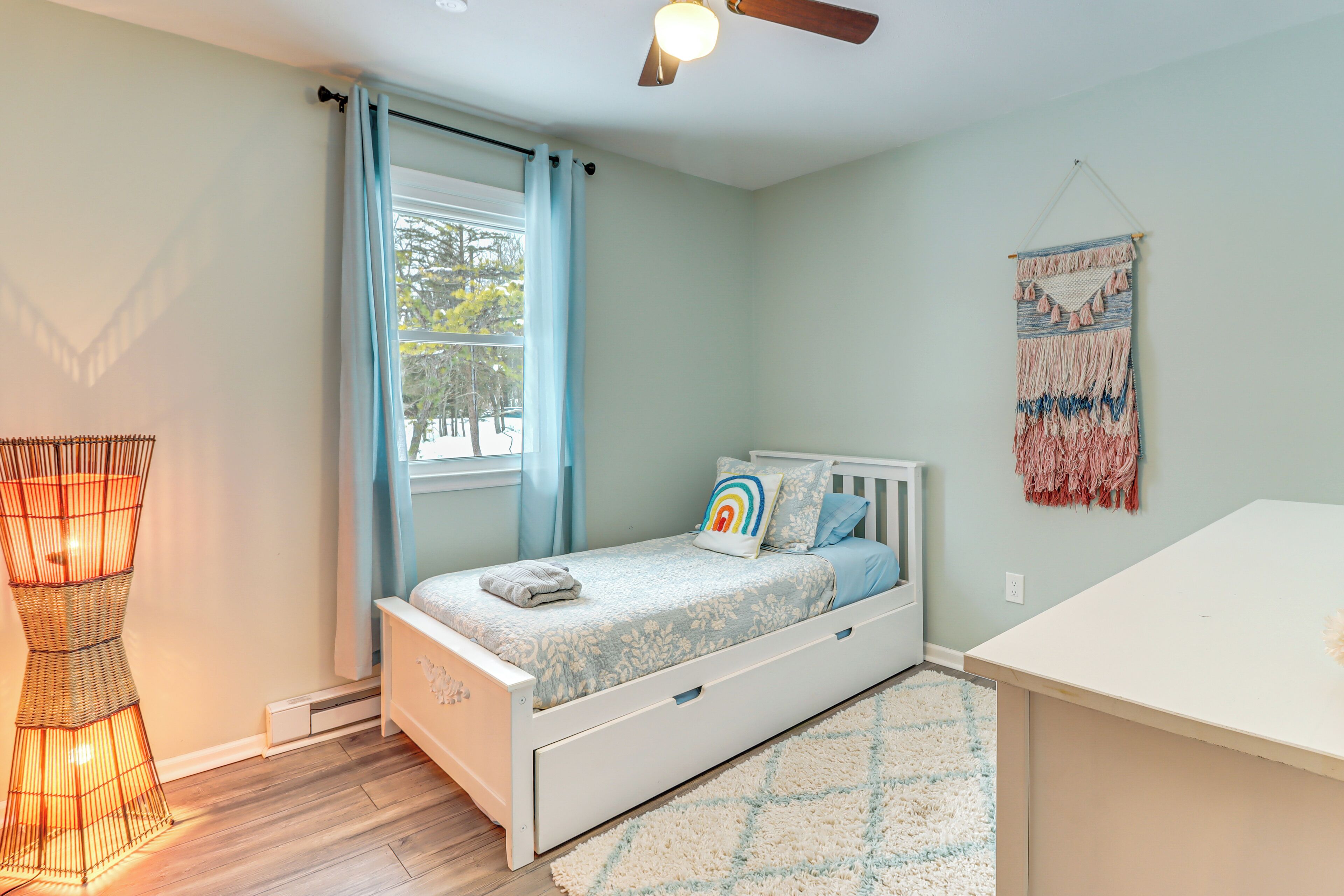 A bedroom with a bed, a bedside table, a hanging tapestry, and a window with curtains.