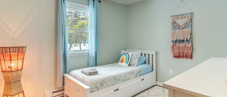 A bedroom with a bed, a bedside table, a hanging tapestry, and a window with curtains.