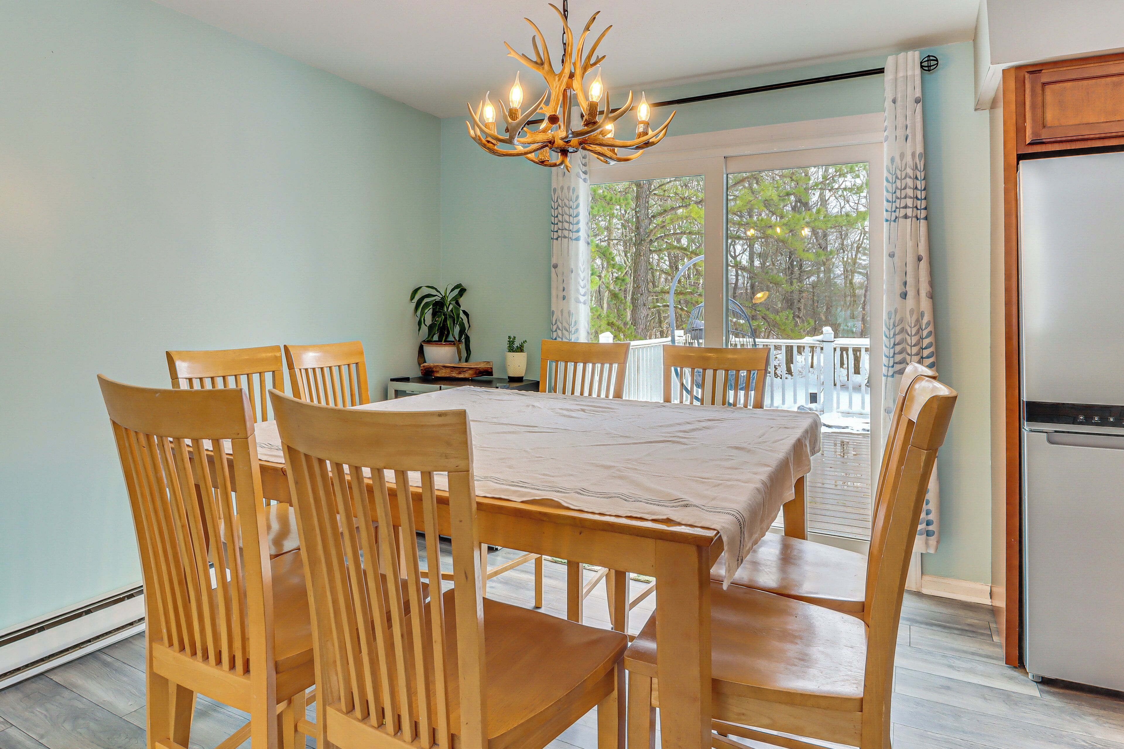 A dining area with a table and chairs, a chandelier, a refrigerator, and a view of the outdoors.