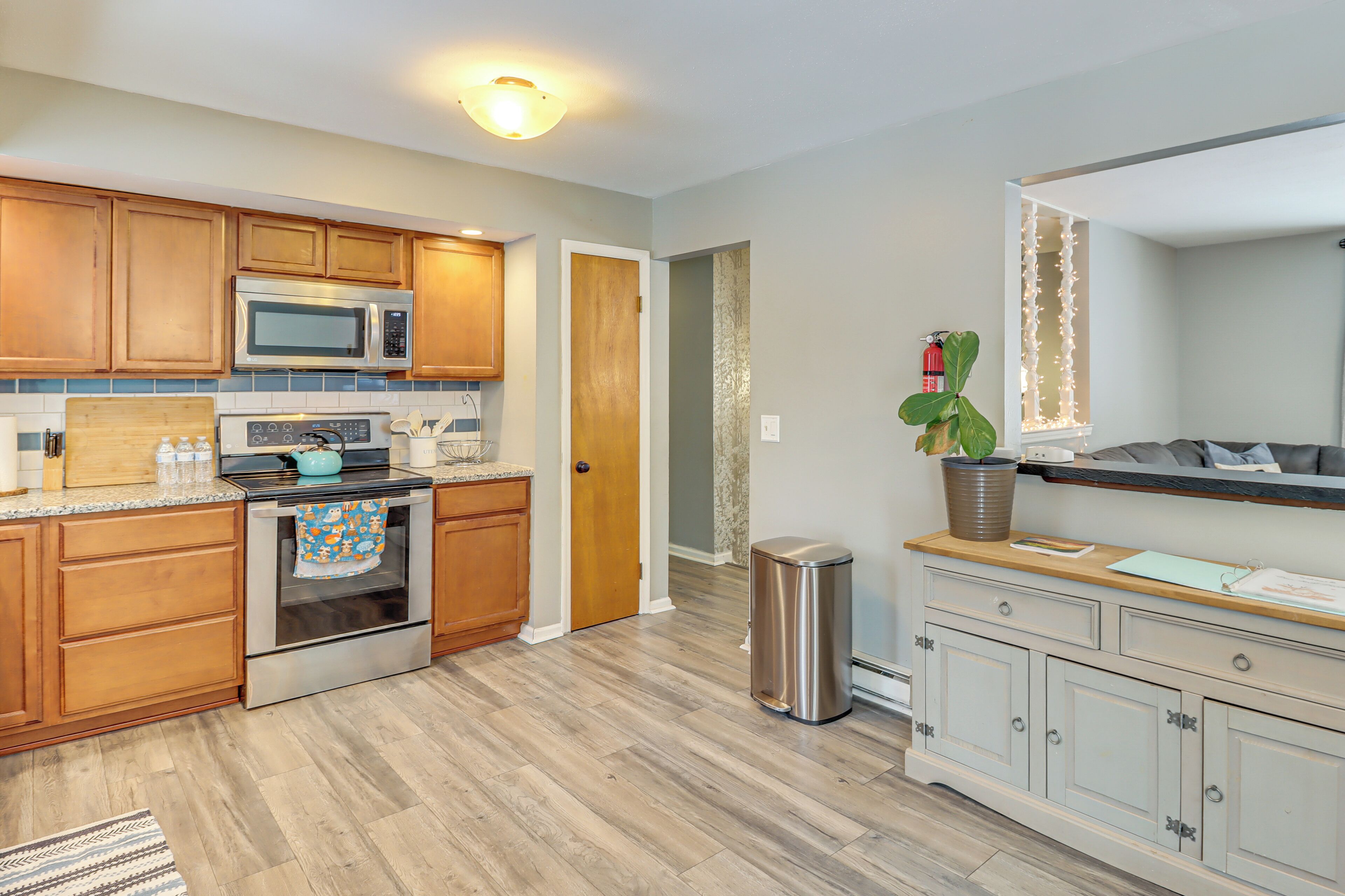 A kitchen with wooden cabinets, a microwave, an oven, a trash can, and a potted plant.