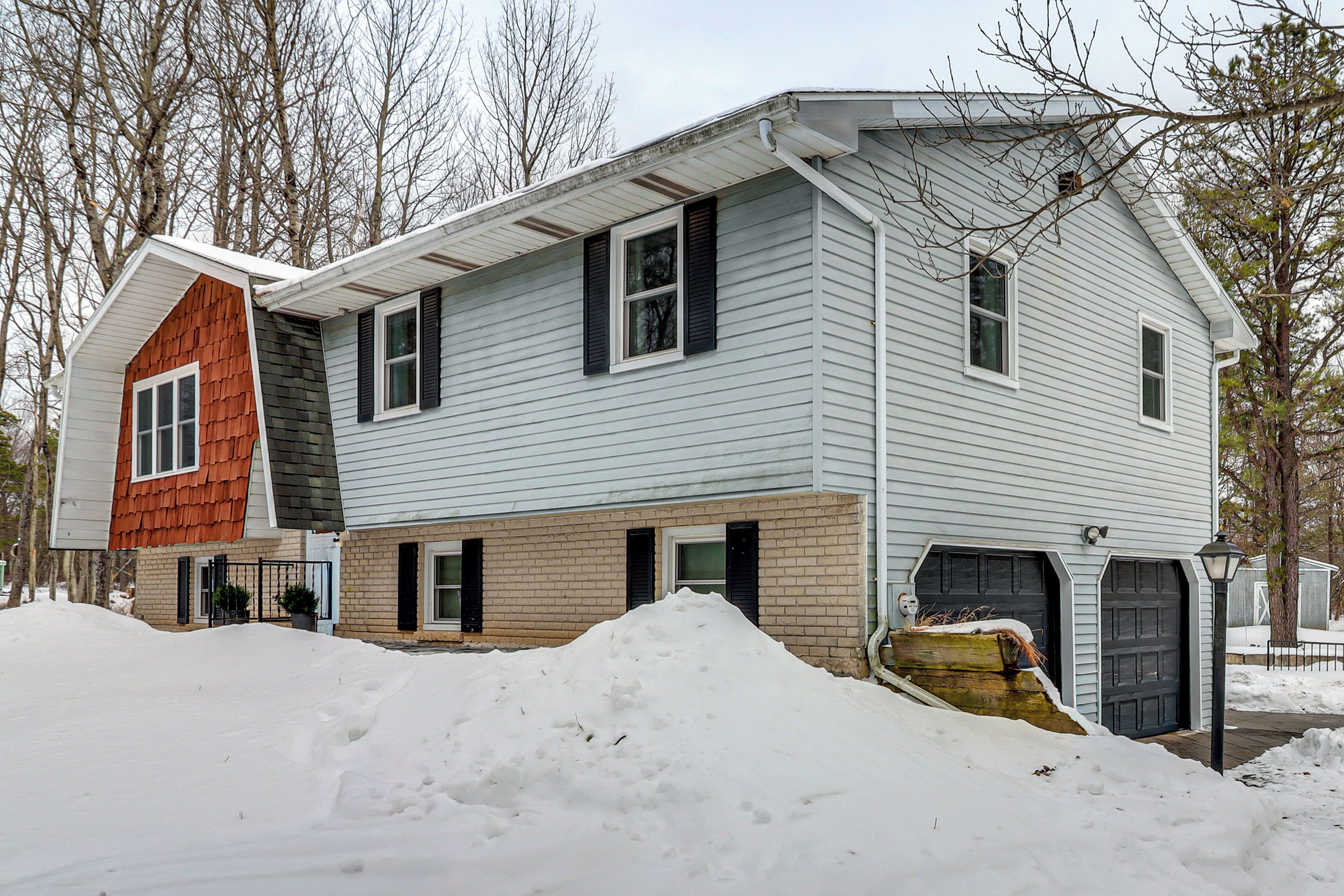A two-story house with a garage, a small shed, and a snow-covered driveway.