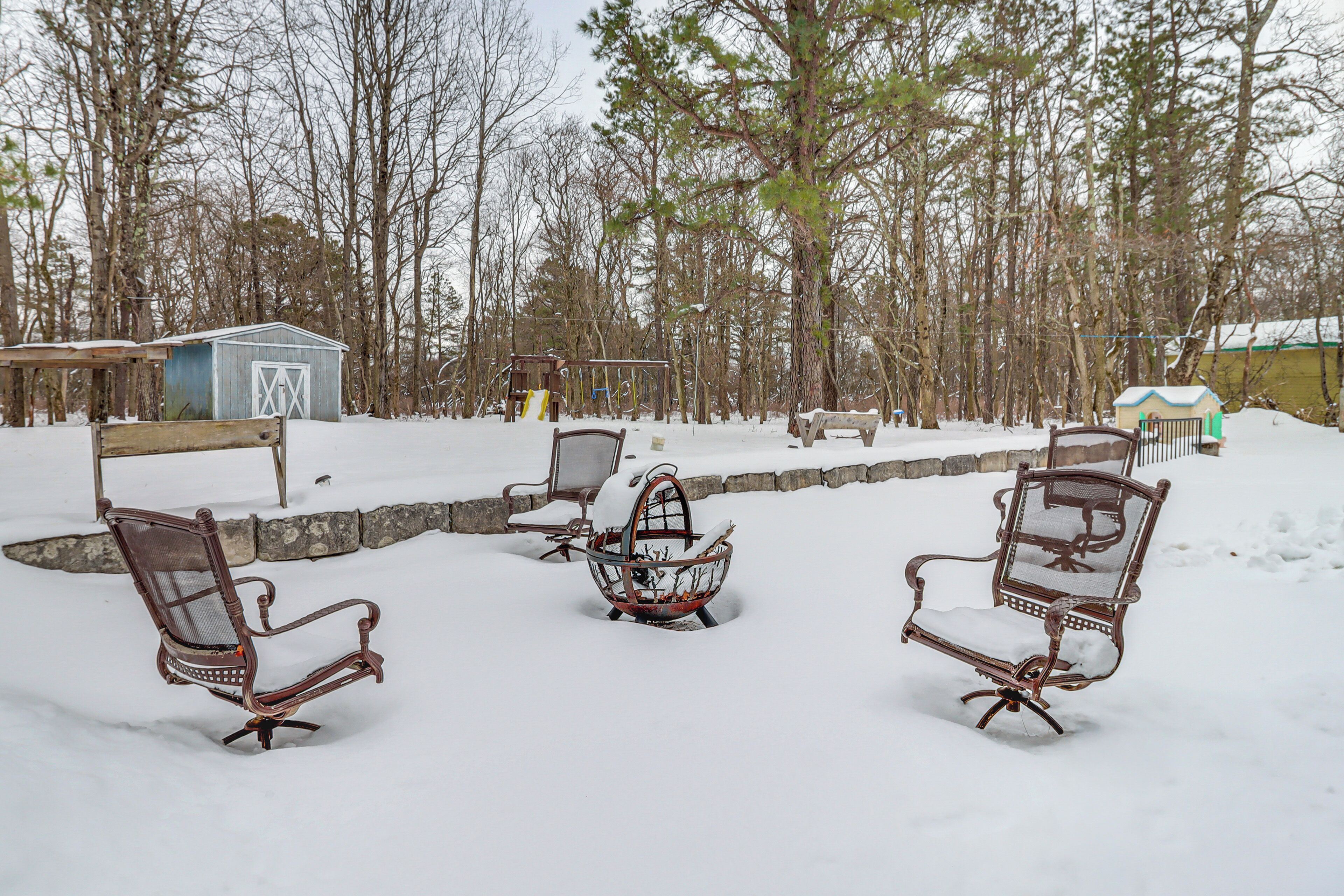 Un espace extérieur aménagé avec des sièges, recouvert de neige, comprenant des chaises en métal et un panier en métal.
