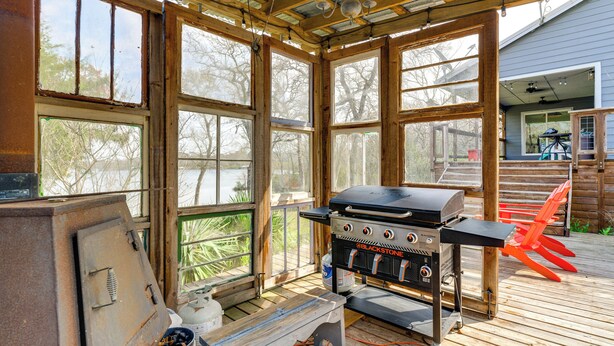 Un espace extérieur abrité comprenant un barbecue, une terrasse en bois et de grandes fenêtres.