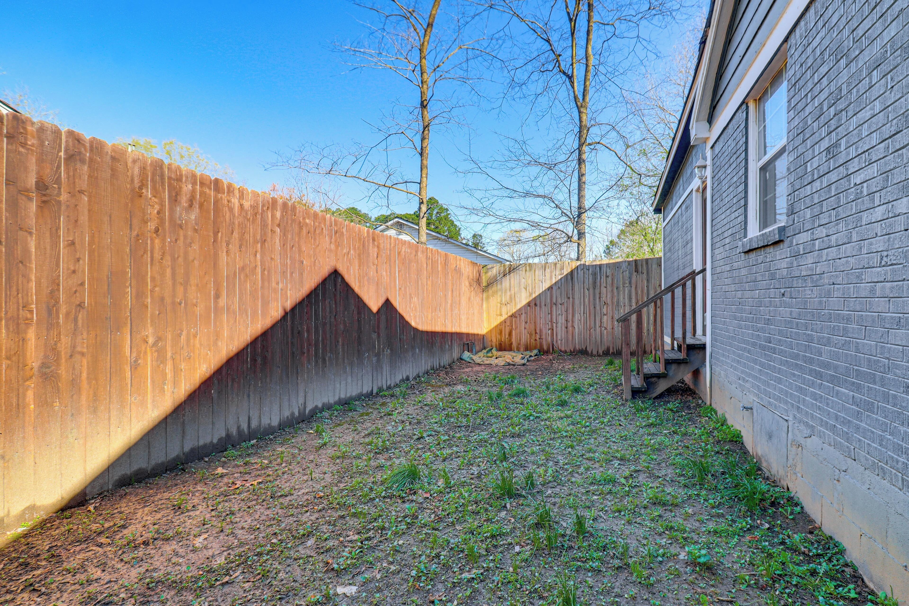 A backyard with a wooden fence, a brick house, and a grassy area.