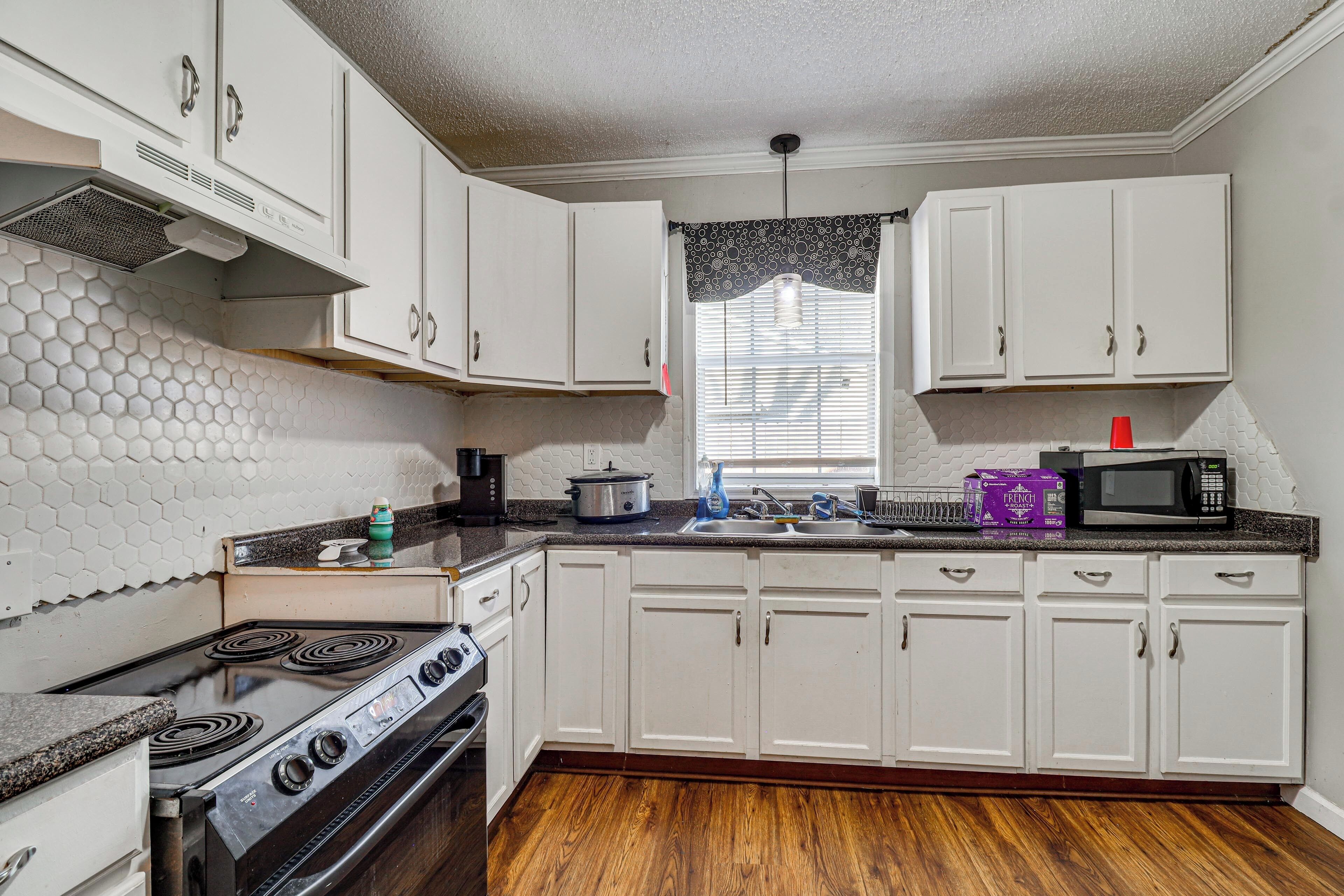 A kitchen with white cabinets, a stove, a microwave, and a window with blinds.