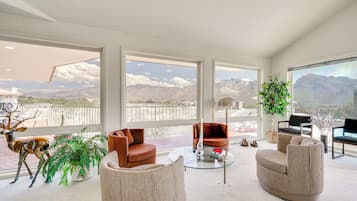 A spacious living room with large windows, a round glass coffee table, and a variety of seating options.