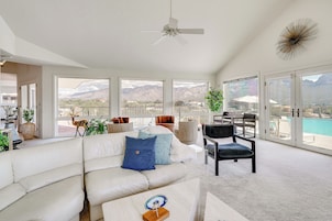 A spacious living room with a white sofa, a ceiling fan, and large windows offering mountain views.