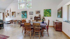 A dining area with a high ceiling, large windows, and artwork on the walls. - Secluded 2 BR Cottage w/ Private W/d, Wifi & Patio (Hancock)