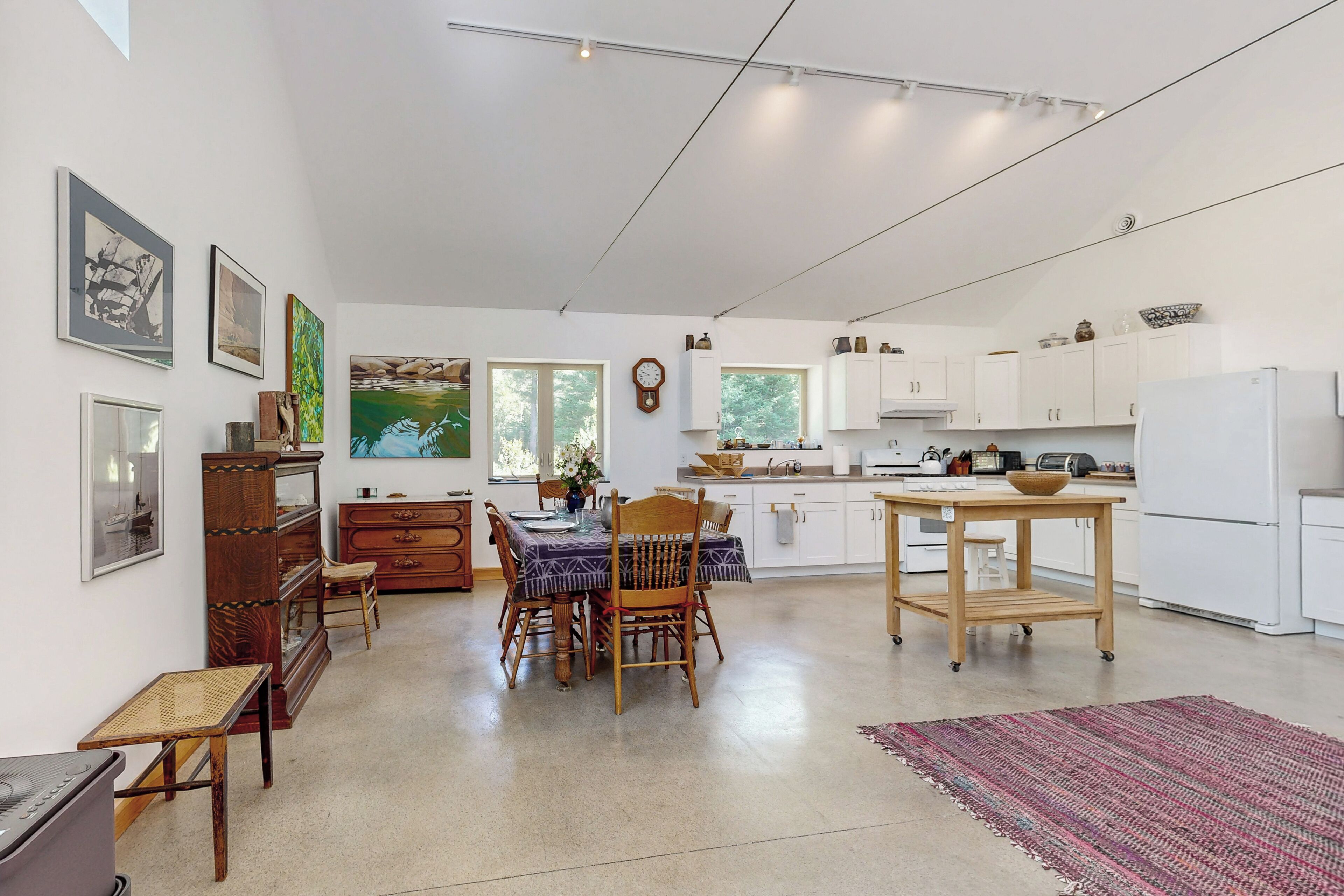 Una cocina amplia con armarios blancos, una mesa de comedor con sillas y un ventanal que proporciona luz natural.