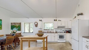 A modern kitchen with white cabinets, a wooden dining table, and a large window. - Secluded 2 BR Cottage w/ Private W/d, Wifi & Patio (Hancock)