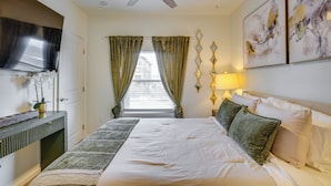 A bedroom with a bed, a ceiling fan, a TV, a window with curtains, and wall art. - Easy Access to Dtwn Tacoma! Stylish Couple's Condo (Tacoma)