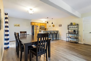 Un comedor con una mesa y sillas de madera, una cocina con armarios de madera y una puerta blanca.