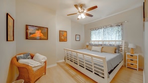 Quarto com cama, uma cadeira, ventoinha no teto e obras de arte nas paredes.