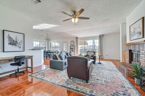 A spacious living room with a fireplace, a ceiling fan, and a large window.