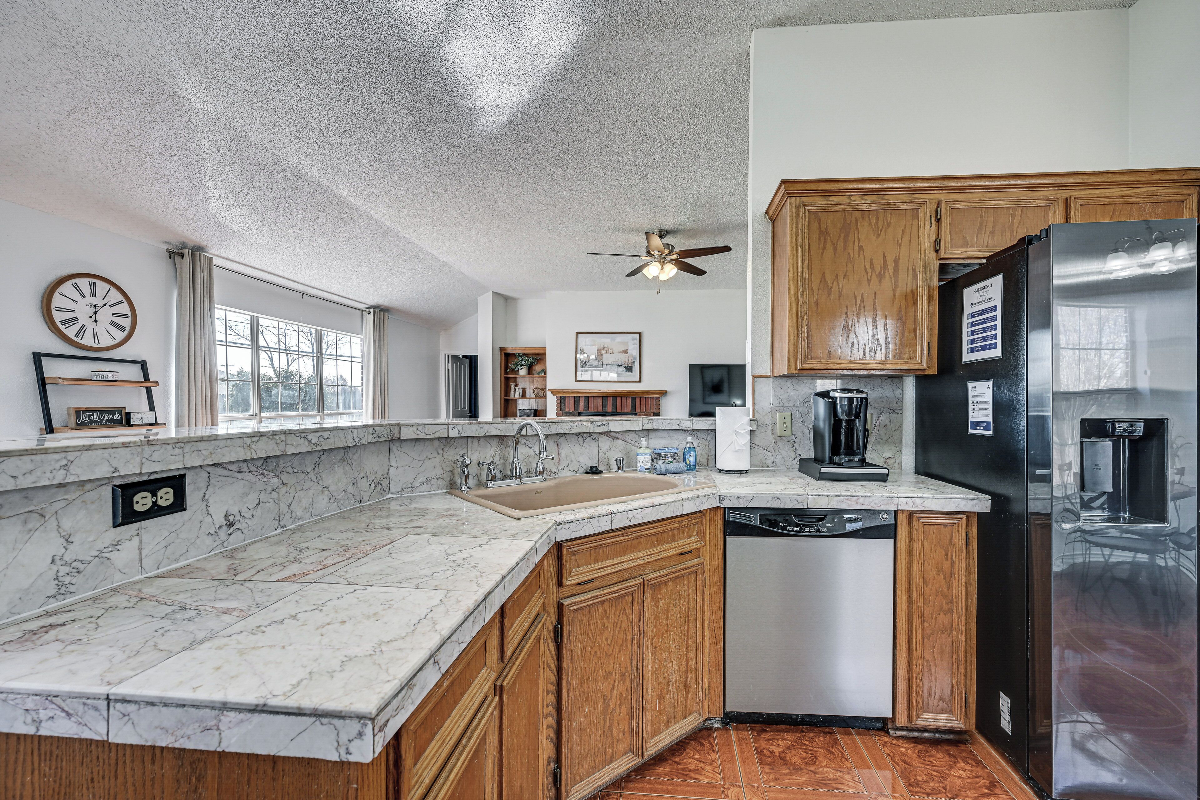 A kitchen with wooden cabinets, a stainless steel refrigerator, a dishwasher, and a marble countertop.