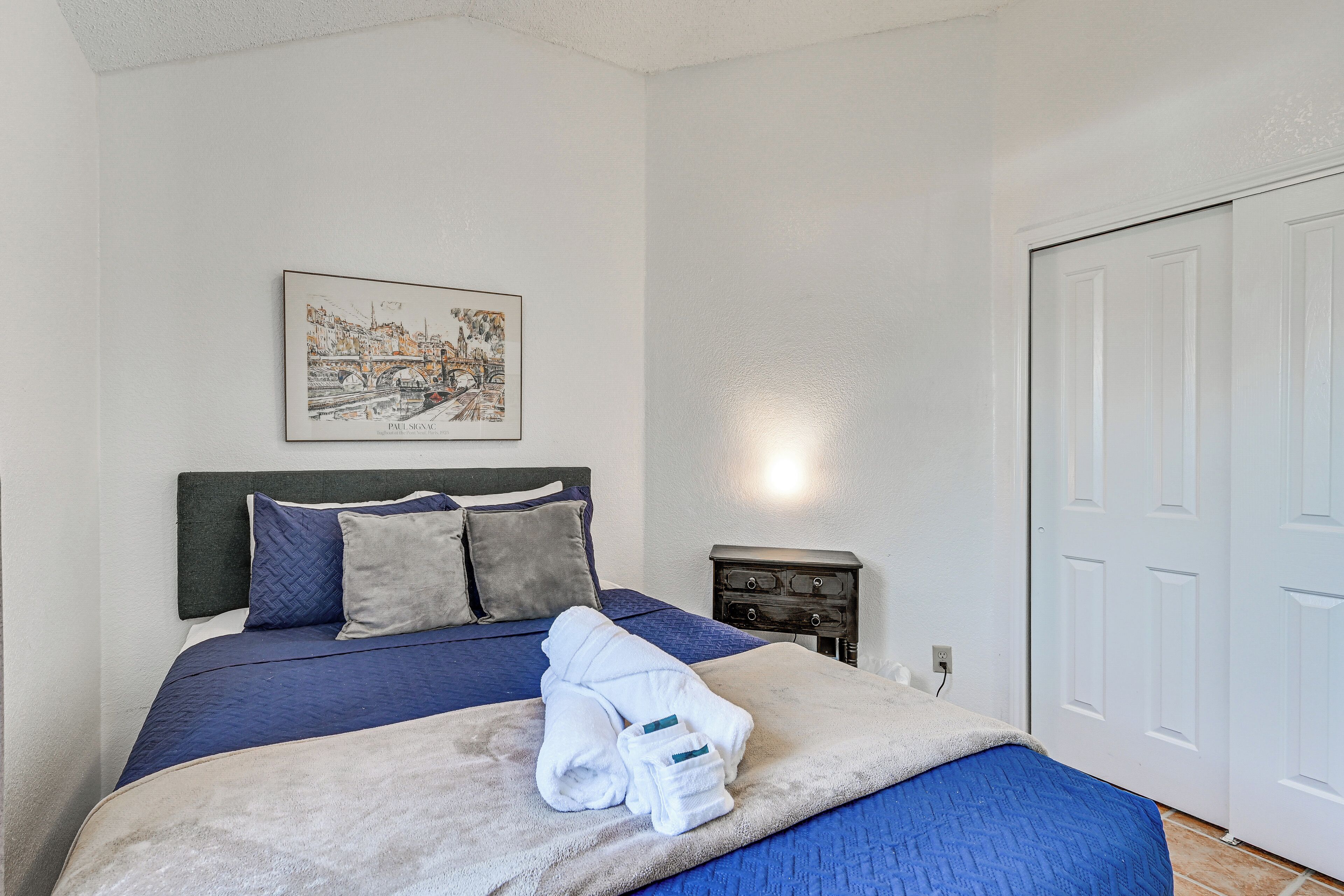 A neatly made bed with a blue and white bedspread, a headboard, and a framed picture on the wall.