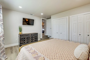 A bedroom with a bed, dresser, TV, and closet.