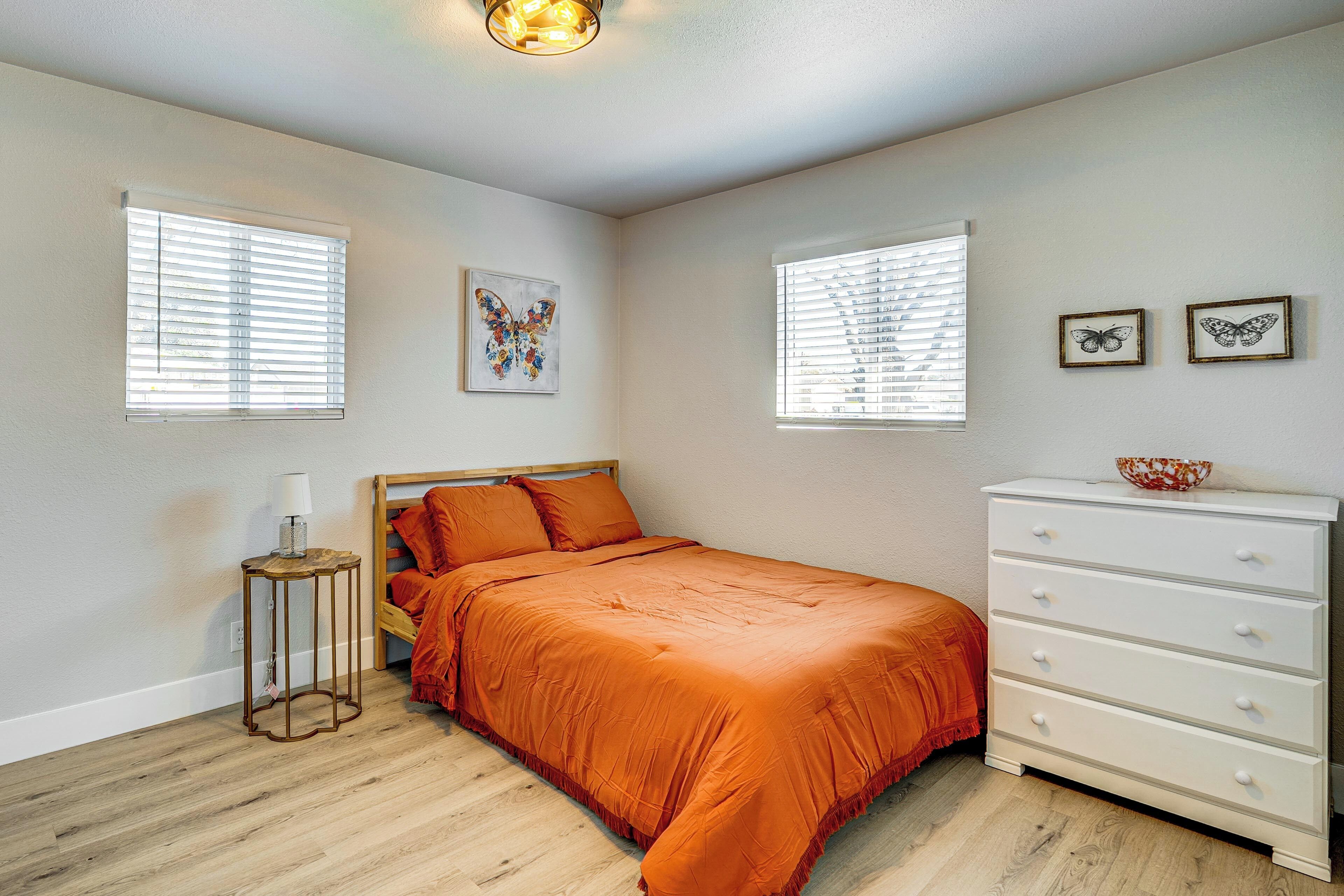 A bedroom with a bed, a dresser, a nightstand, and two windows with blinds.