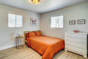 A bedroom with a bed, a dresser, a nightstand, and two windows with blinds.