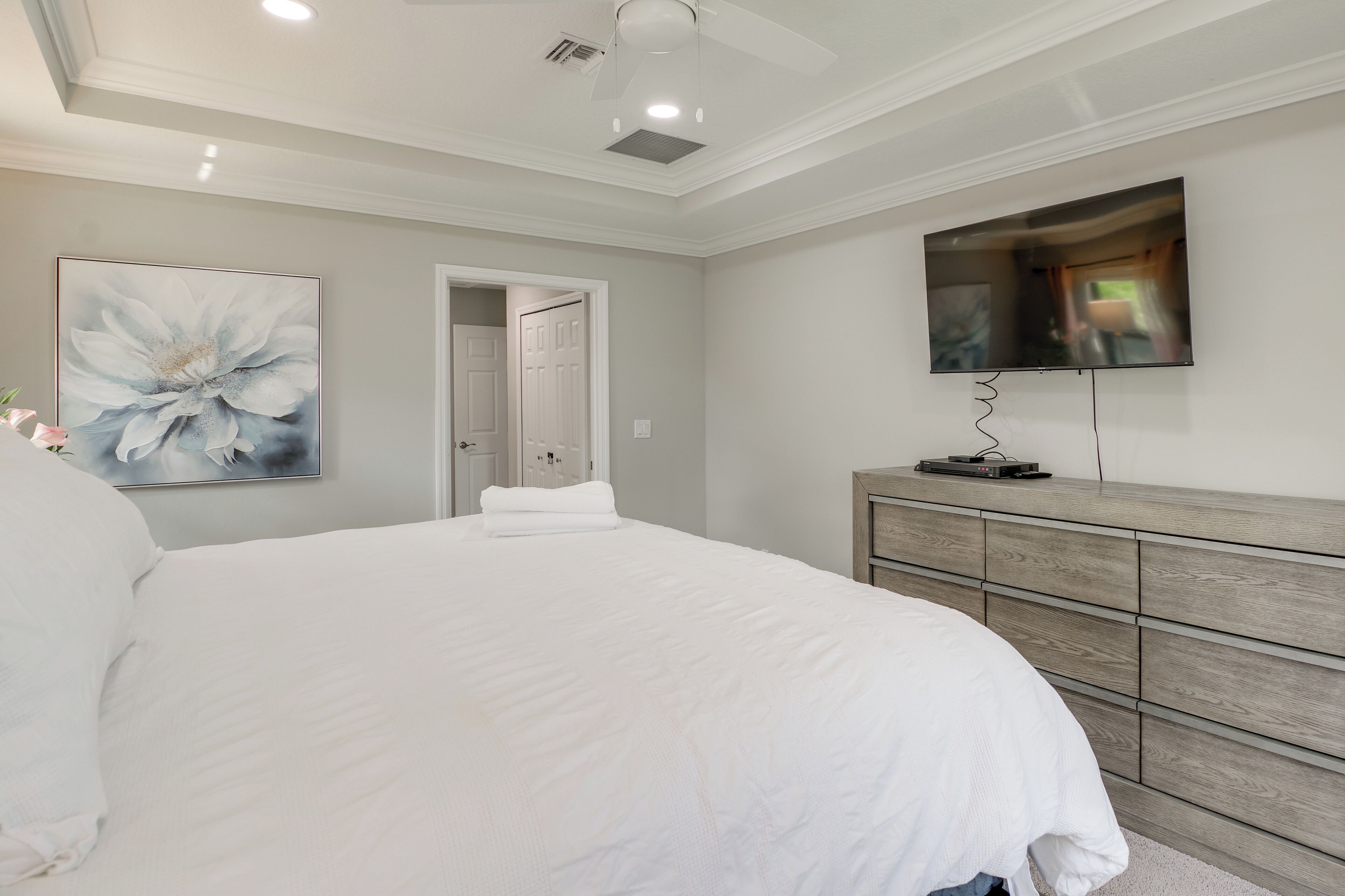 Un dormitorio con una cama grande, un televisor de pantalla plana montado en la pared, un aparador de madera y una puerta que da a otra habitación.