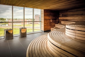A modern interior with large windows, a curved wooden bench, and a view of a building across the street. - Make Your Trip More Enjoyable! 2 Relaxing Units, Onsite Parking and Dining! (Helmond)