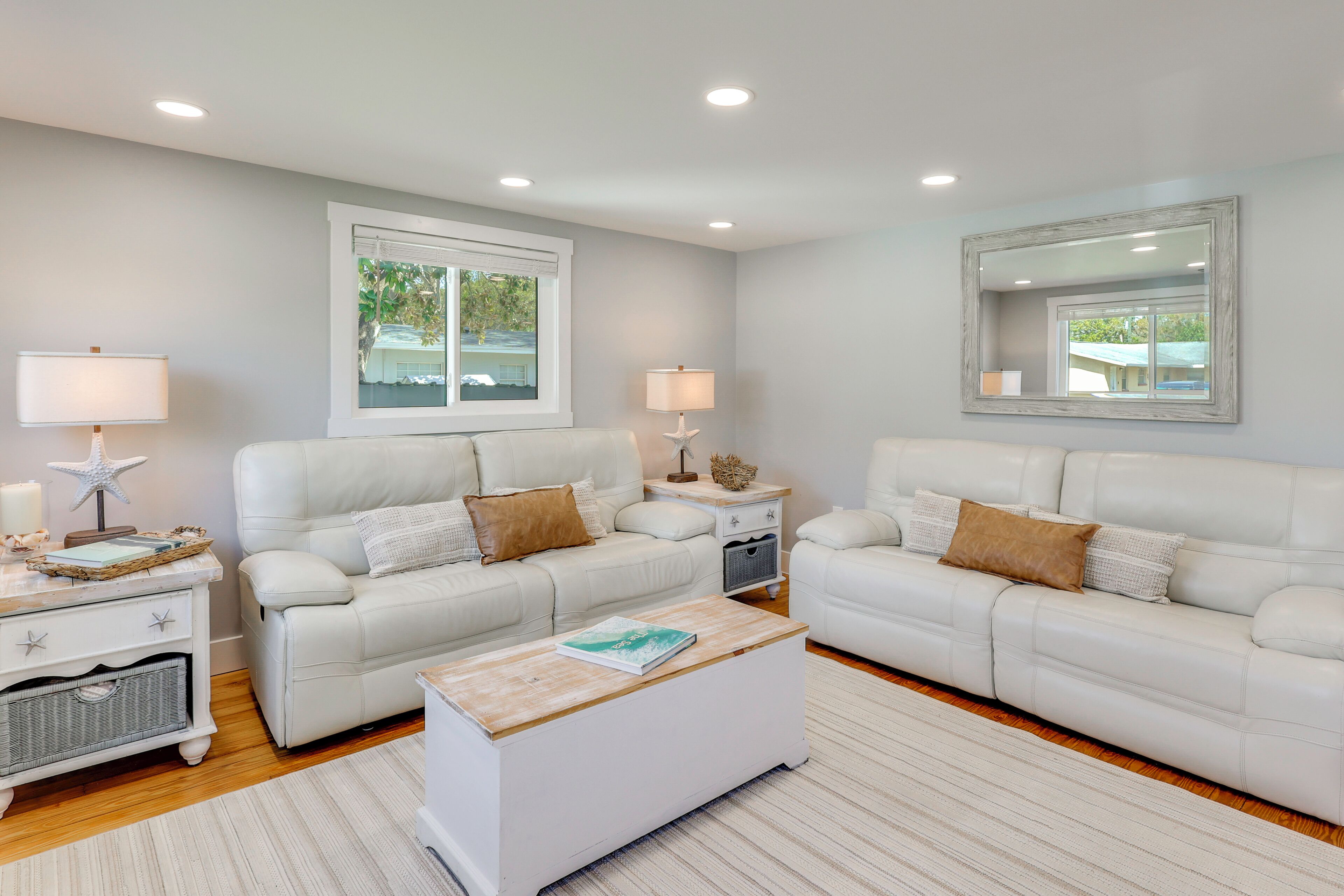 A modern living room with two white leather sofas, a wooden coffee table, and a white side table with lamps.