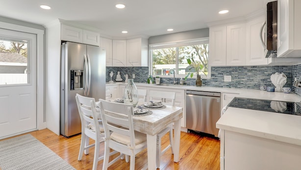 A modern kitchen with white cabinetry, a stainless steel refrigerator, a dining table with chairs, and a window providing natural light. - 7 Mi to Indian Rocks Beach: Breezy Family Retreat! (Largo)