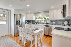 A modern kitchen with white cabinetry, a stainless steel refrigerator, a dining table with chairs, and a window providing natural light. - 7 Mi to Indian Rocks Beach: Breezy Family Retreat! (Largo)