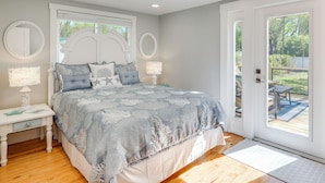 A bedroom with a bed, nightstands, and a view of an outdoor patio. - 7 Mi to Indian Rocks Beach: Breezy Family Retreat! (Largo)
