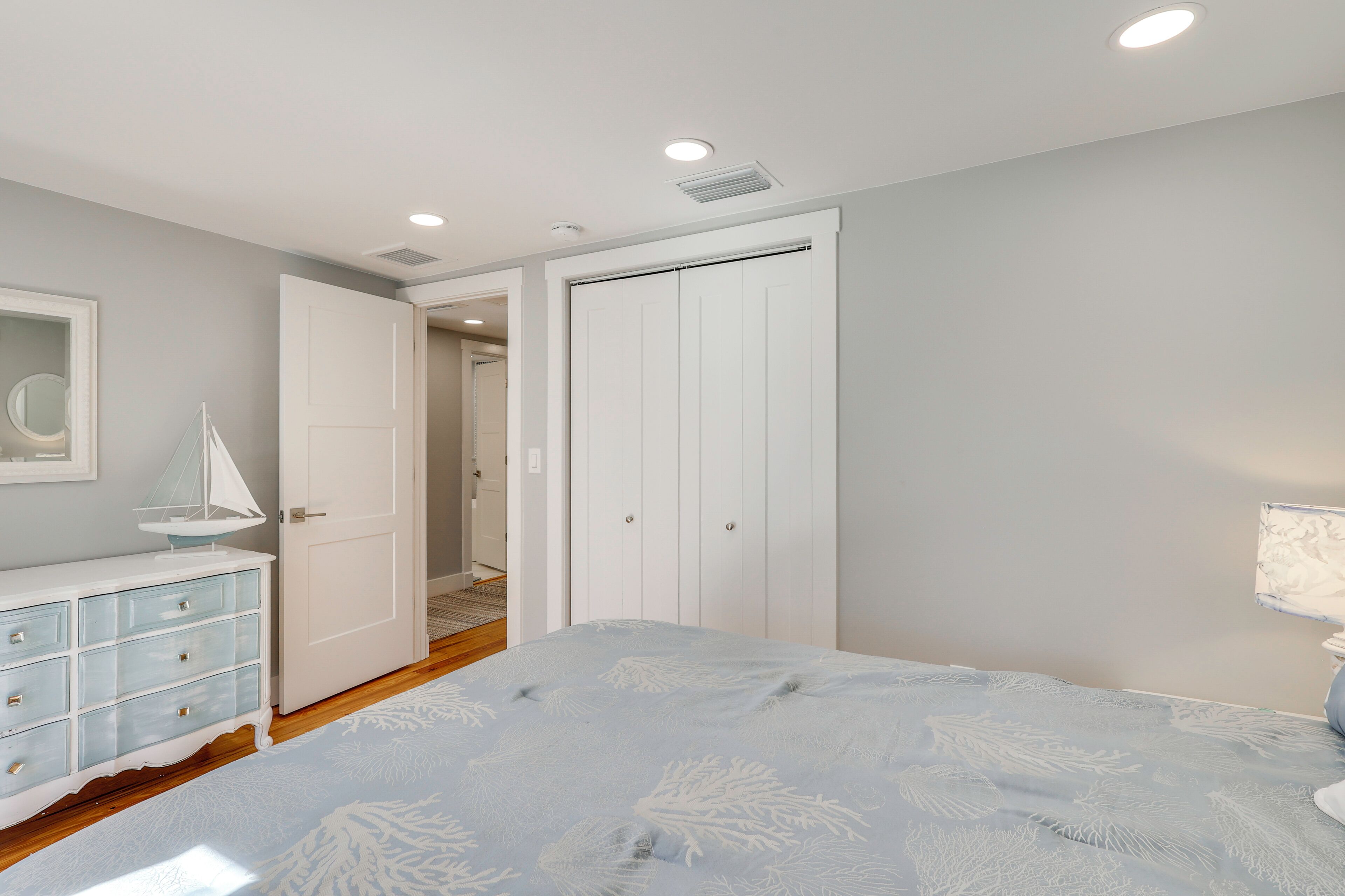 A bedroom with a bed, a dresser, a door, and a lamp.