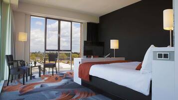 A hotel room with a bed, a TV, a desk, a chair, and a view of the outdoors.