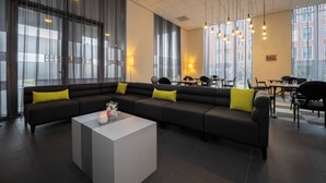 Eine moderne Hotelhalle mit einer schwarzen Eckcouch, einem weißen Couchtisch und einem Essbereich mit Tischen und Stühlen.