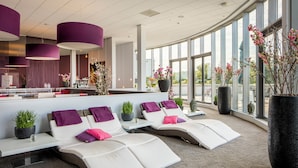 A modern lounge area with reclining chairs, a reception desk, and large windows. - Ensuring a Very Comfortable & Memorable Stay! Parking (Helmond)