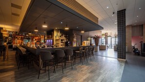 A bar area with a long counter, multiple bar stools, and a variety of bottles and glasses.