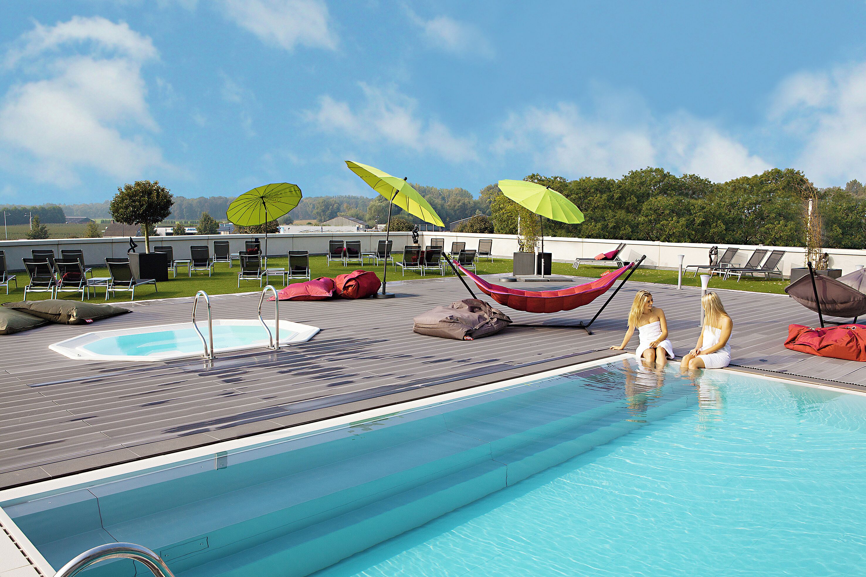 Zwembad met ligbedden en parasols, een kleine jacuzzi, en een houten terras.
