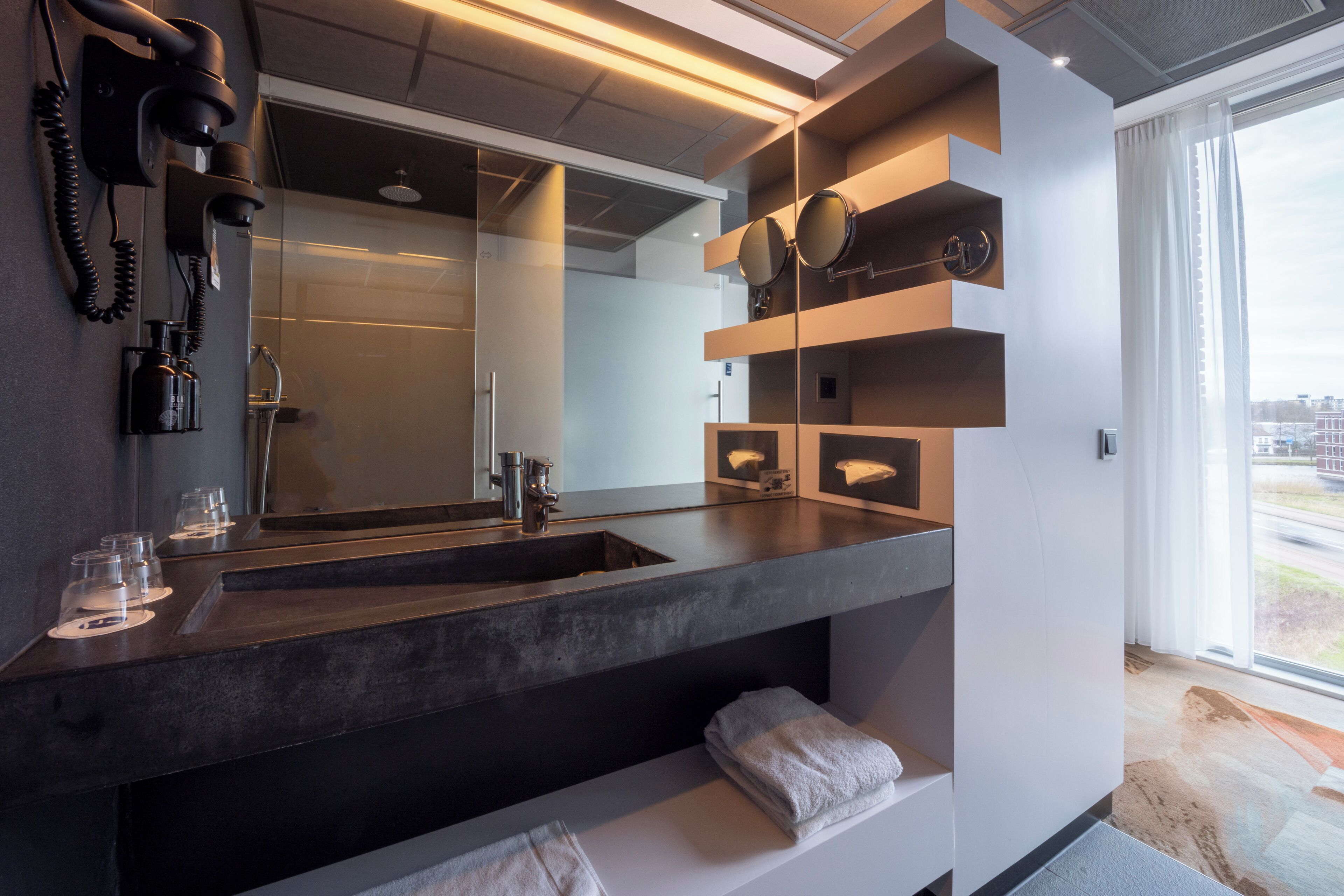 Een moderne badkamer met een grote spiegel, donkere aanrechtbladen en een inloopdouche.