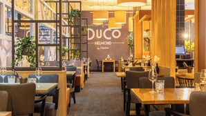 A restaurant interior with tables, chairs, and a wall with the name 'DUCO HELMOND by Fletcher'. - Modern Helmond Stay | 1 Unit | Near City Center (Helmond)