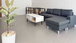 Un salon moderne avec un canapé d’angle gris, une table d’appoint blanche et une plante en pot.