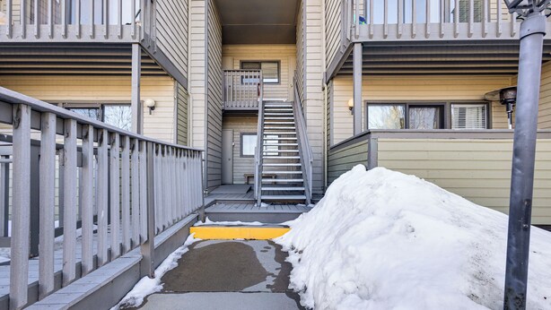 Un étroit passage entre deux bâtiments, avec une rambarde métallique d’un côté et une zone recouverte de neige de l’autre.
