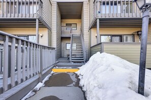 Un étroit passage entre deux bâtiments, avec une rambarde métallique d’un côté et une zone recouverte de neige de l’autre.