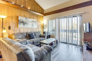 A living room with a sectional sofa, a coffee table, a painting, a TV, and a balcony with a view. - Shuttle to Winter Park Resort: Mtn-view Condo! (Fraser)
