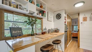 A kitchen with a wooden countertop, bar stools, a window with a view, shelves with kitchen items, and a clock on the wall. - 5 Mi to Mt Rainier Park: Unique & Rustic Getaway (Ashford)