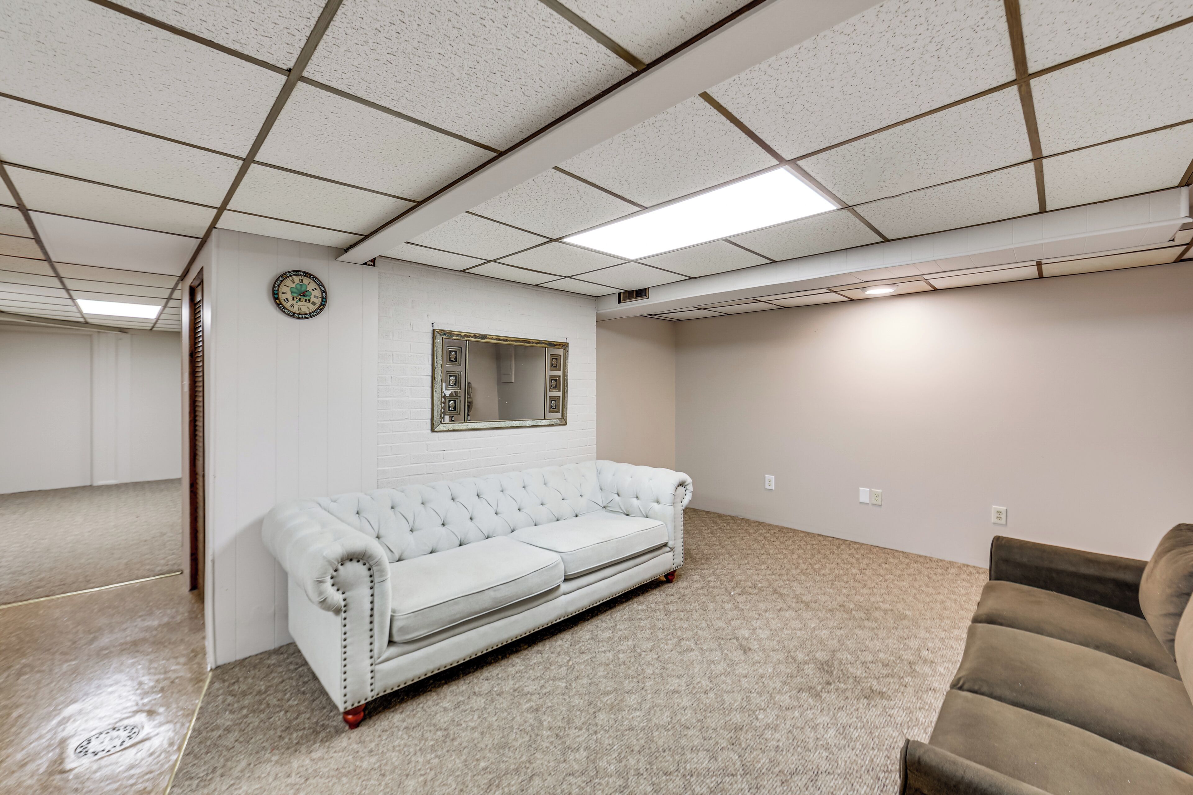 A room with a white tufted sofa, a brown sofa, a mirror, and a clock on the wall.