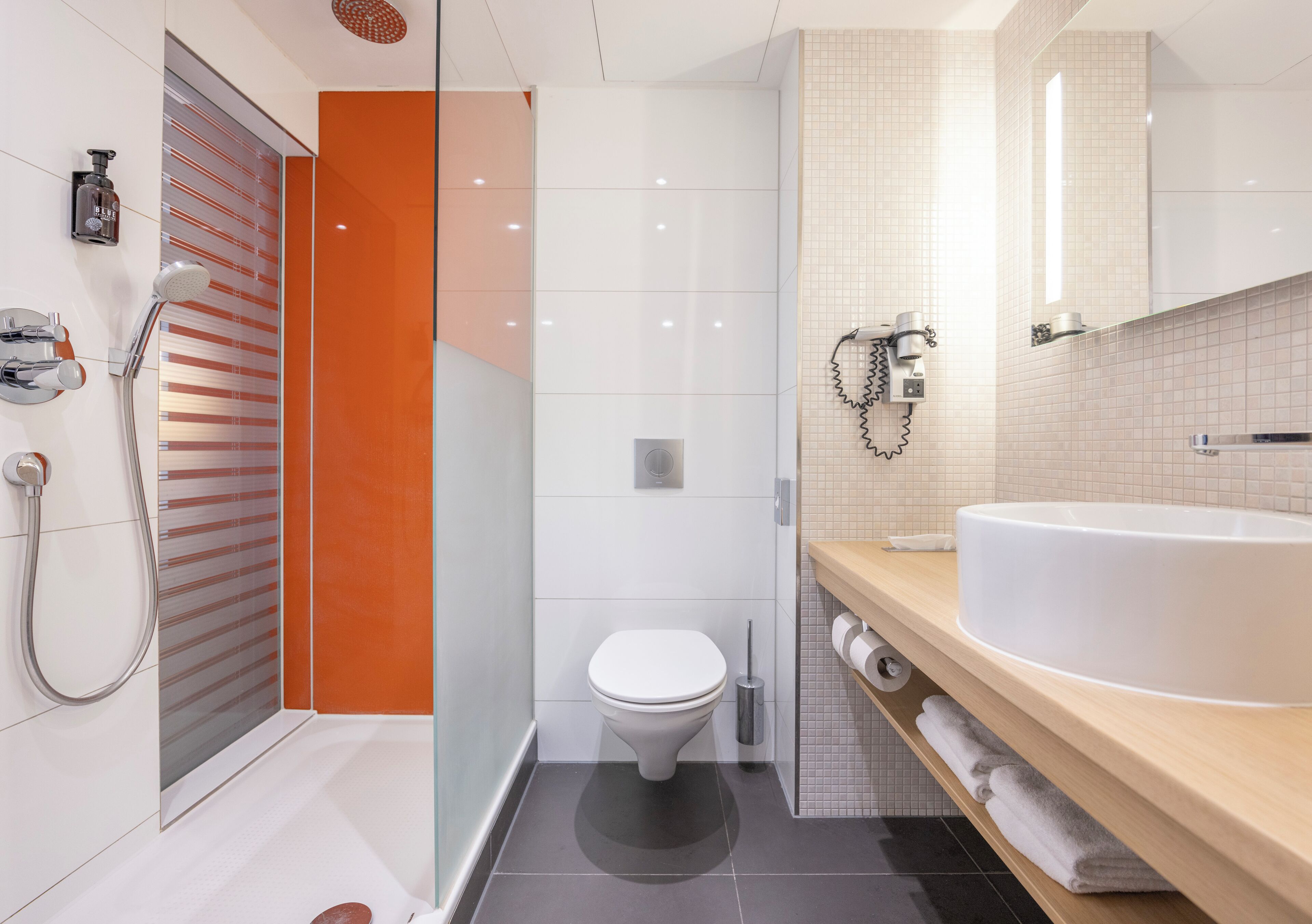 Ein modernes Badezimmer mit Duschkabine aus Glas, einer weißen Toilette, einem großen Waschbecken und einem Spiegel darüber.