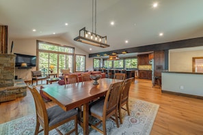 A spacious dining area with a wooden table and chairs, a stone fireplace, and large windows offering views of the outdoors. - 4BR Home w/ 2 Decks, Near Lake & Ski Resorts (Truckee)